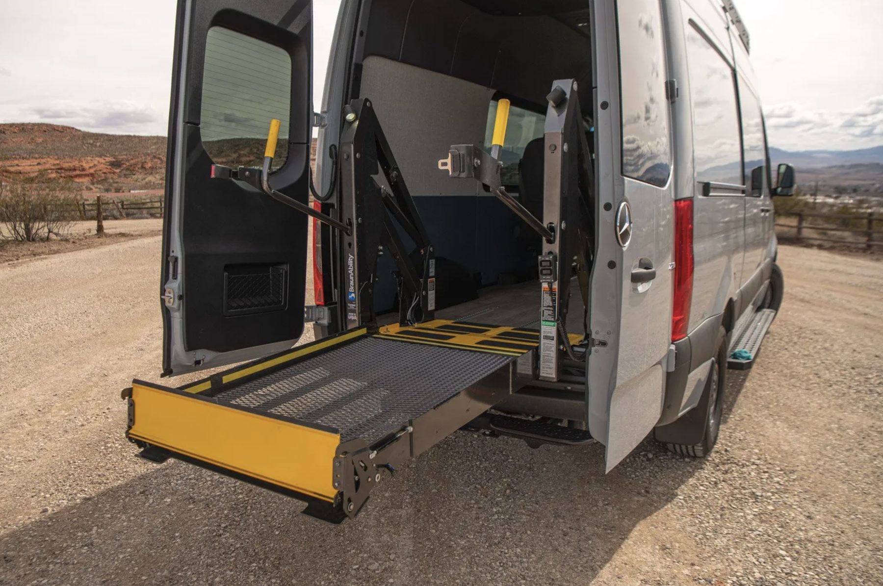A BraunAbility platform lift extended through the open rear doors of a Sprinter and lowered flat to the ground.