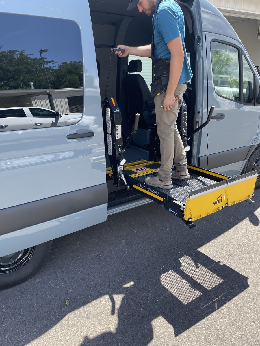 The technician standing on the deployed lift platform, holding the pendant control on its coiled cable and watching the platform as he runs it through its travel.