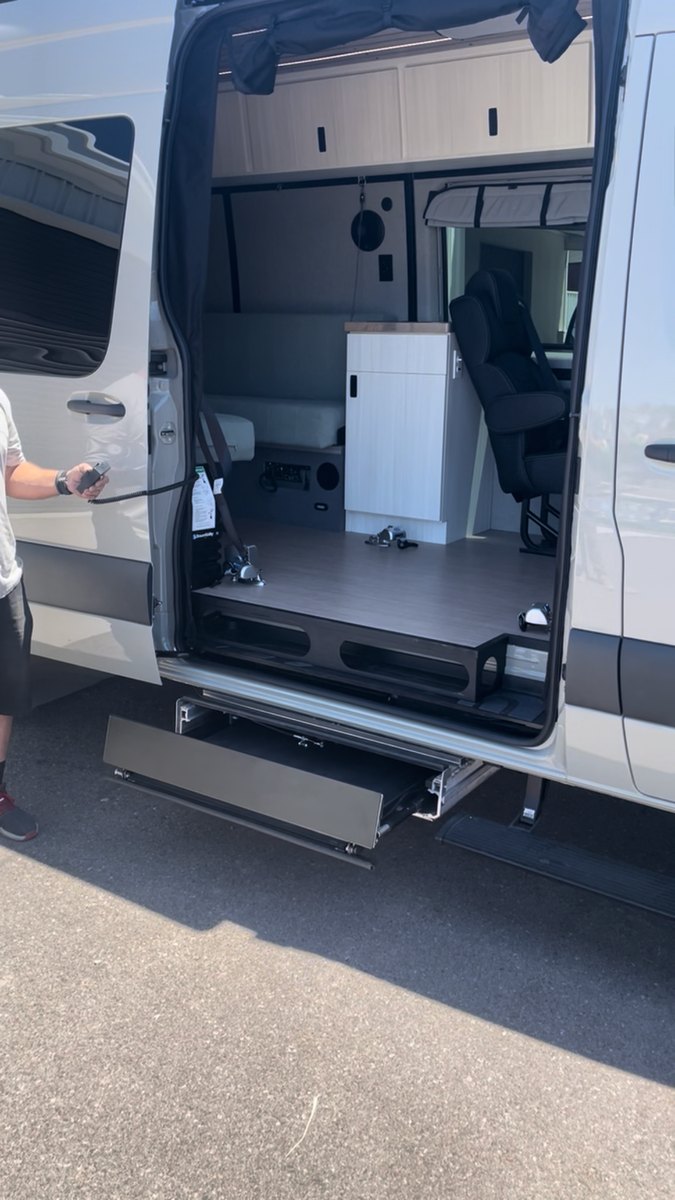 The lift cassette sliding out horizontally from beneath the van floor, still folded flat, while a technician holds the pendant control at the side of the vehicle.