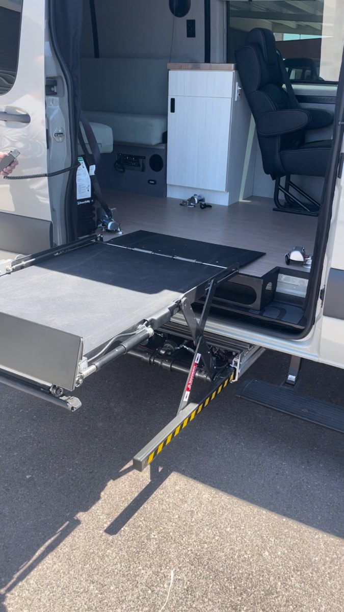 The lift unfolding: the platform has opened out on its scissor arms below the door sill, with the van&rsquo;s interior, galley cabinet and captain&rsquo;s chair visible through the open door.