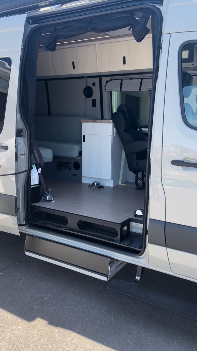 The open side door of a custom Sprinter with the under-vehicle lift fully stowed: the doorway and the van&rsquo;s wood floor are completely clear, with only the securement anchors visible and the cassette hidden beneath the floor.