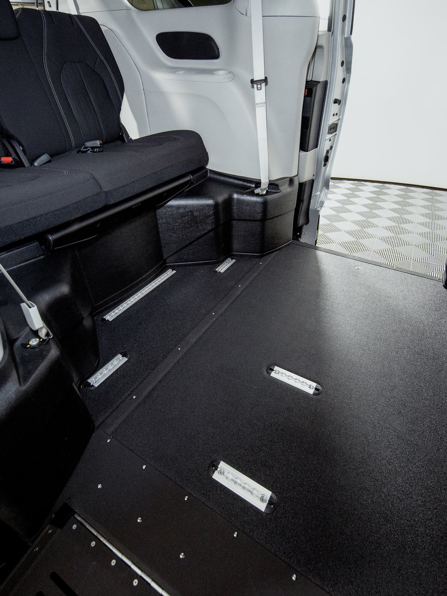 The lowered floor of a Pacifica Northstar seen from the open side door: a flat wheelchair bay beside the rear bench seat, with securement track and recessed floor fittings set into it.