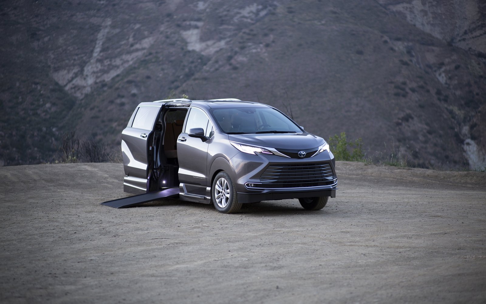 A white Toyota Sienna facing the camera on a snow-covered road between frosted trees, headlights on, under a heavy sky.