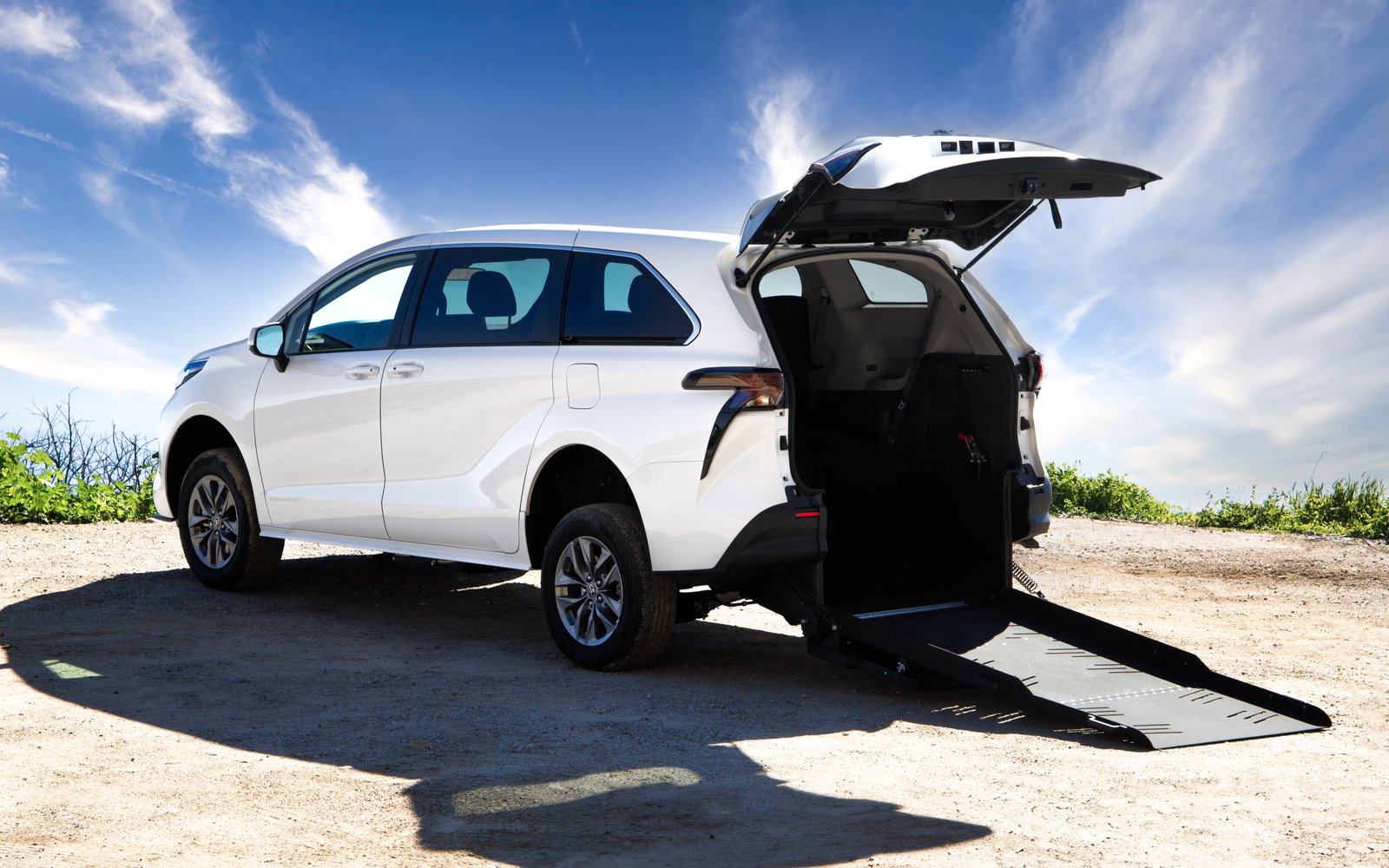 A Toyota Sienna Rear Entry in profile in an accessible bay, tailgate raised and the ramp folded out behind the vehicle onto the ground.